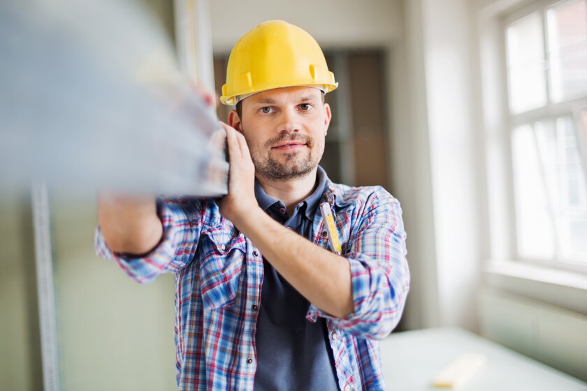 Bauarbeiter mit Helm bei Einbau von Fenstern auf Baustelle.