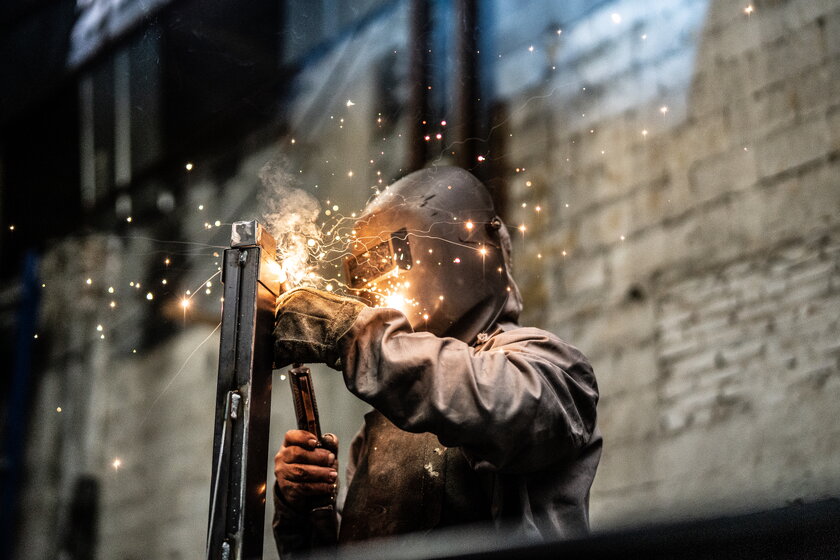 Ein Mann im Arbeitsanzug mit Schutzmaske beim Schweissen von Metall.