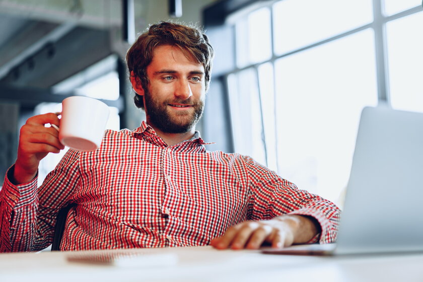 Smarter junger Mann mit Bart in legerem Hemd vor seinem Laptop.