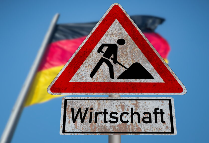 Flagge von Deutschland weht hinter Verkehrsschild Baustelle Wirtschaft.