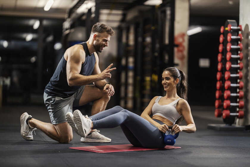 Sportlerin beim Kettlebell-Twist, Trainer unterstuetzt motivierend.