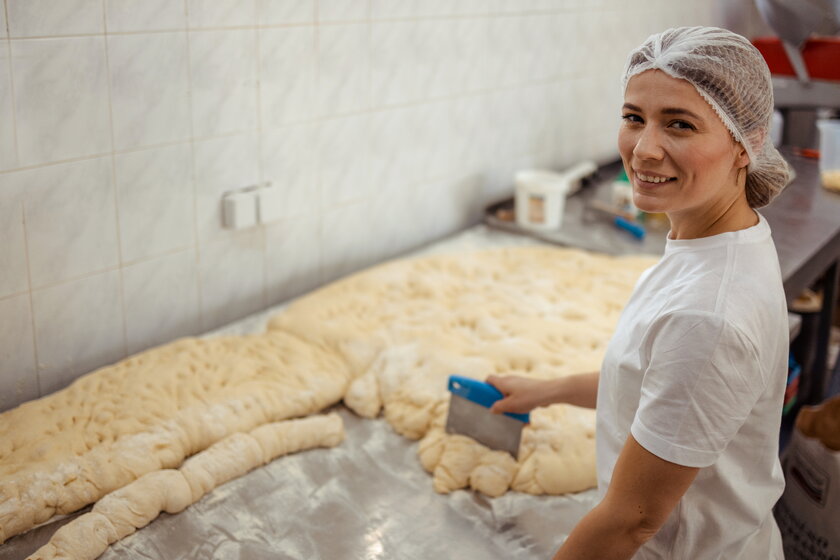 Professionelle Baeckerin bereitet frisches Brot in der Backstube zu.